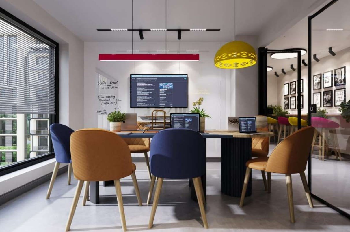 Open collaborative table with pastel chairs beside a gallery wall