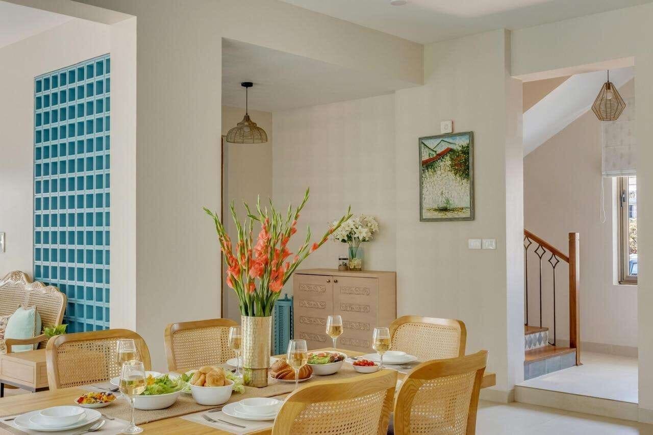 Dining area with cane chairs and fresh flowers, staircase beyond